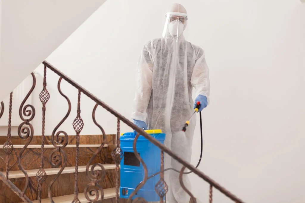man spreading disinfectant against covid 19 wearing biohazard costume scaled 1